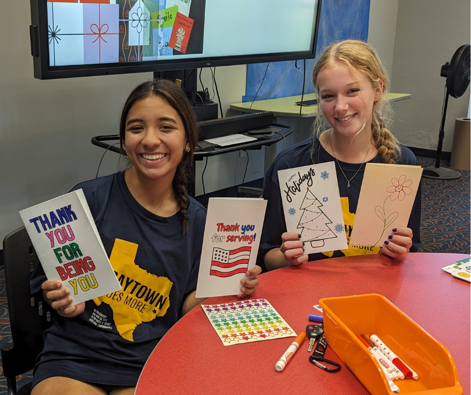Two women holding decorated cards. 